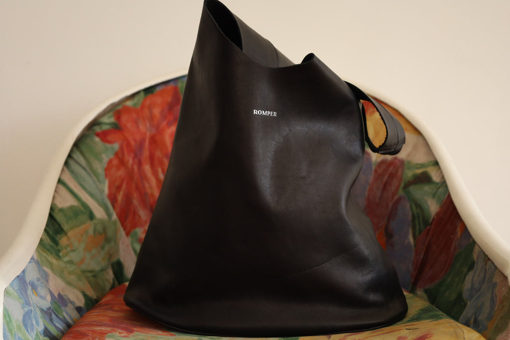 Black smooth leather Margarita Large with silver embossed logohandbag front part resting on a vintage chair.