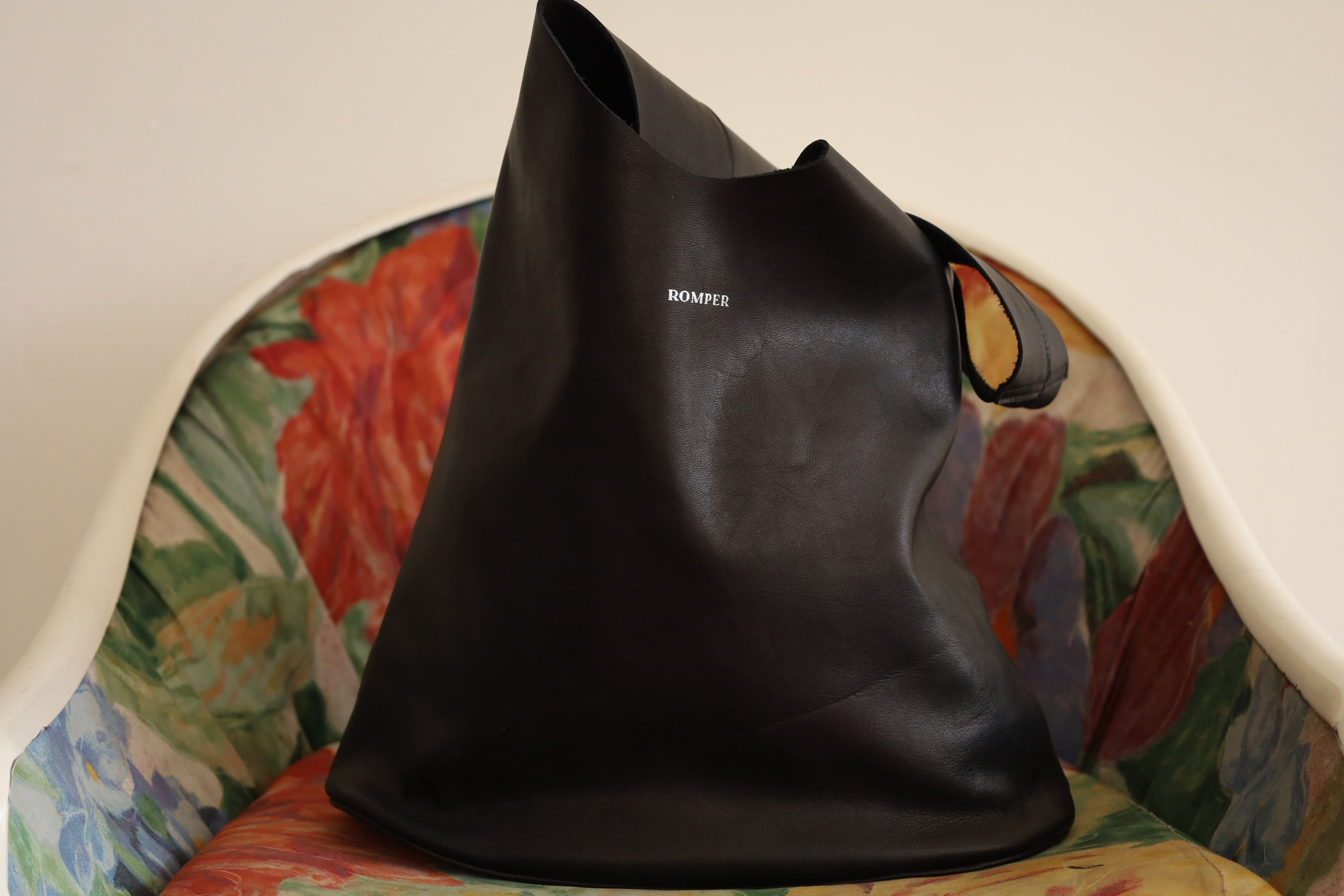 Black smooth leather Margarita Large with silver embossed logohandbag front part resting on a vintage chair.